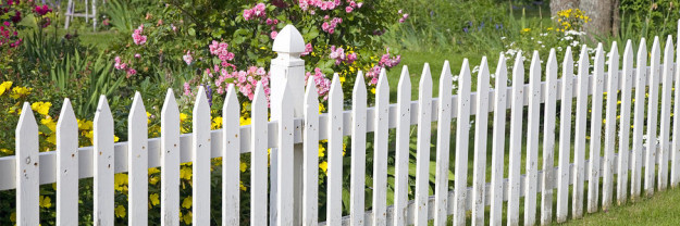 Rustic white picket fence with roses and other flowers in the background. white picket fence with flowers and garden
